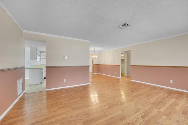 empty room featuring visible vents, an inviting chandelier, crown molding, a textured ceiling, and light wood-style floors