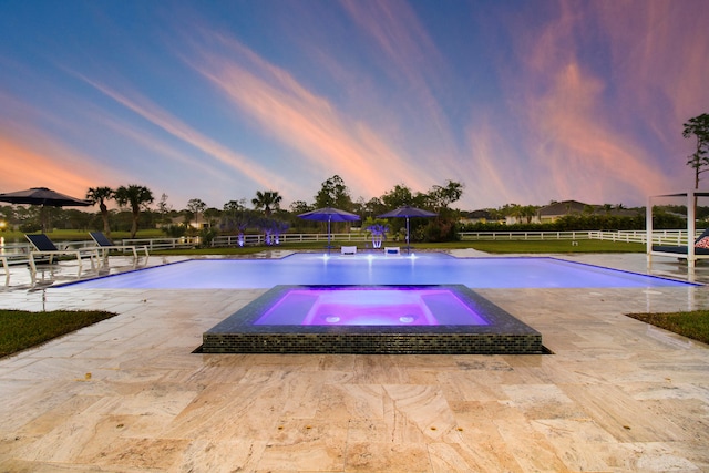 pool at dusk with an in ground hot tub and a patio area