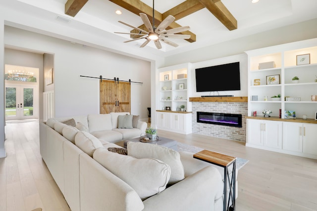 living room featuring a fireplace, a barn door, light wood-type flooring, and beam ceiling