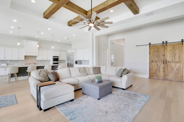 living room with light wood-type flooring, beam ceiling, a barn door, and ceiling fan