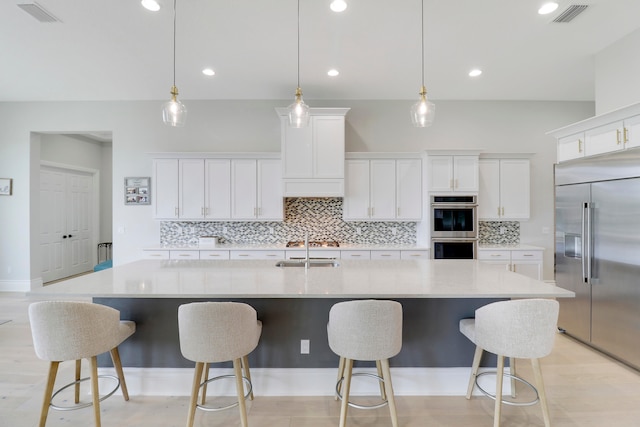 kitchen featuring appliances with stainless steel finishes, white cabinetry, a large island with sink, and pendant lighting