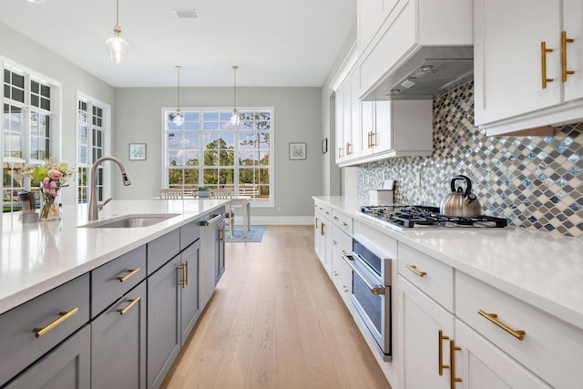 kitchen with gray cabinetry, pendant lighting, premium range hood, sink, and appliances with stainless steel finishes