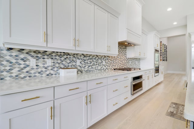 kitchen with white cabinets, backsplash, stainless steel appliances, and light hardwood / wood-style floors