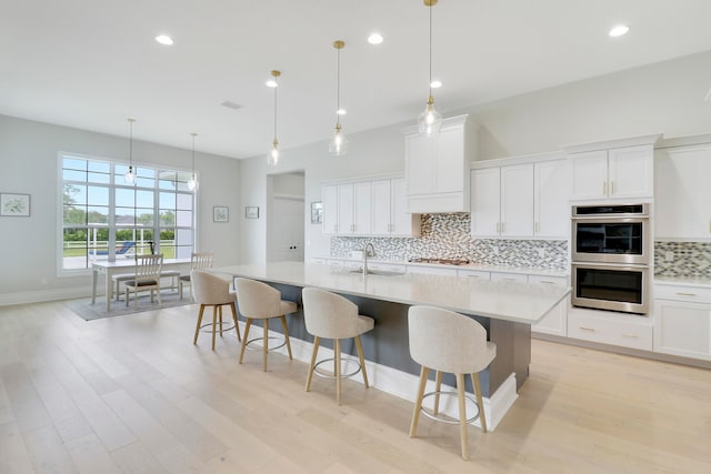 kitchen featuring a center island with sink, white cabinets, light hardwood / wood-style flooring, and appliances with stainless steel finishes