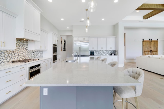 kitchen with a large island, stainless steel appliances, a barn door, light hardwood / wood-style flooring, and a kitchen bar