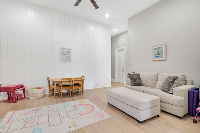 living room with ceiling fan, light hardwood / wood-style flooring, and wooden walls