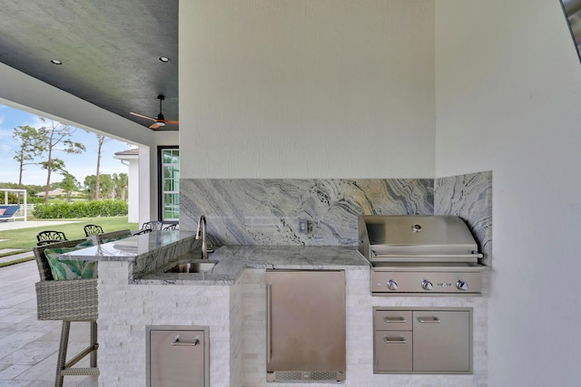 view of patio / terrace with a wet bar, an outdoor kitchen, ceiling fan, and a grill