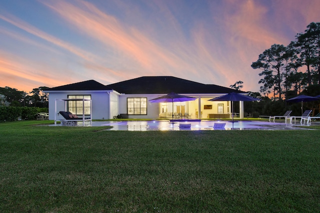 back house at dusk with a lawn and a patio