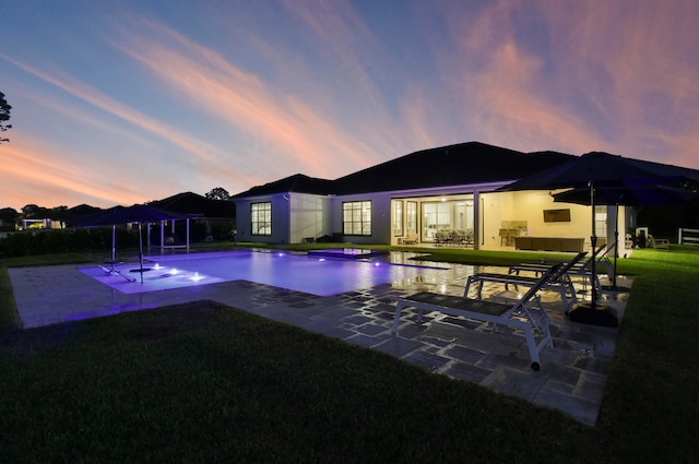 pool at dusk featuring a patio area and a yard