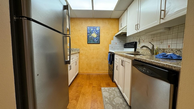 kitchen with sink, white cabinetry, appliances with stainless steel finishes, light stone counters, and light hardwood / wood-style floors