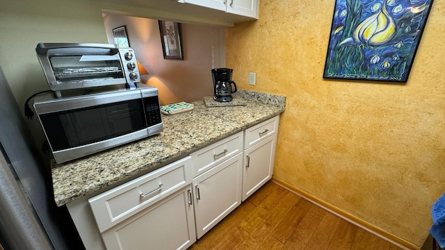 kitchen featuring white cabinetry, hardwood / wood-style floors, and light stone counters