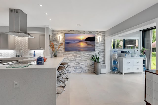 kitchen featuring gray cabinetry, sink, a kitchen bar, island exhaust hood, and kitchen peninsula