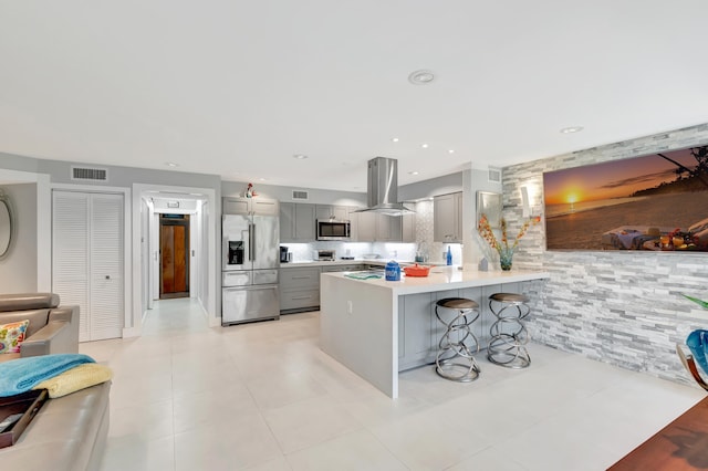 kitchen with a breakfast bar area, island exhaust hood, appliances with stainless steel finishes, and gray cabinetry