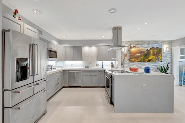 kitchen featuring gray cabinets, island exhaust hood, appliances with stainless steel finishes, and tasteful backsplash