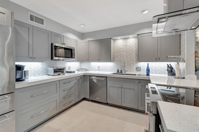 kitchen featuring gray cabinets, appliances with stainless steel finishes, light stone countertops, and backsplash