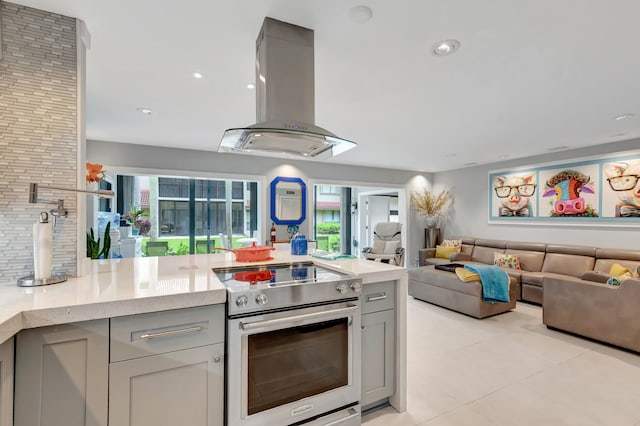 kitchen with island range hood, gray cabinetry, light tile patterned floors, light stone counters, and stainless steel electric range oven