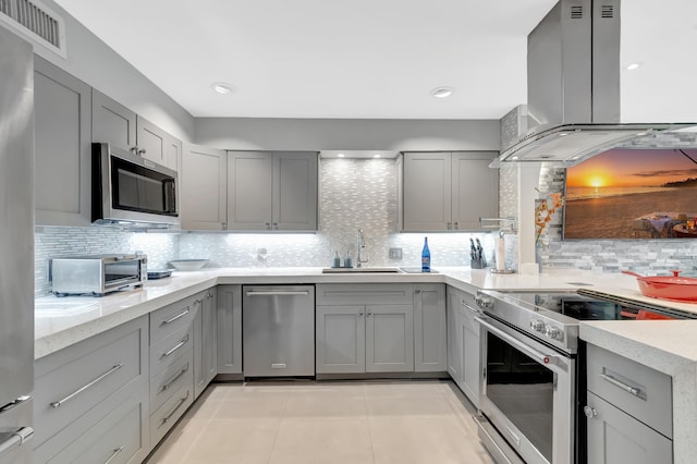 kitchen featuring wall chimney range hood, decorative backsplash, appliances with stainless steel finishes, gray cabinetry, and sink