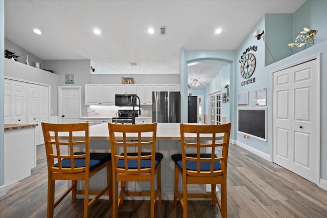 kitchen featuring appliances with stainless steel finishes, a kitchen breakfast bar, white cabinetry, light hardwood / wood-style floors, and a center island with sink