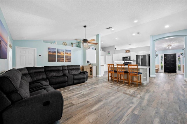 living room with light hardwood / wood-style floors, a textured ceiling, lofted ceiling, and ceiling fan