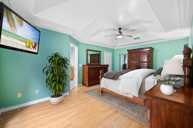 bedroom with ornamental molding, light hardwood / wood-style flooring, a tray ceiling, and ceiling fan