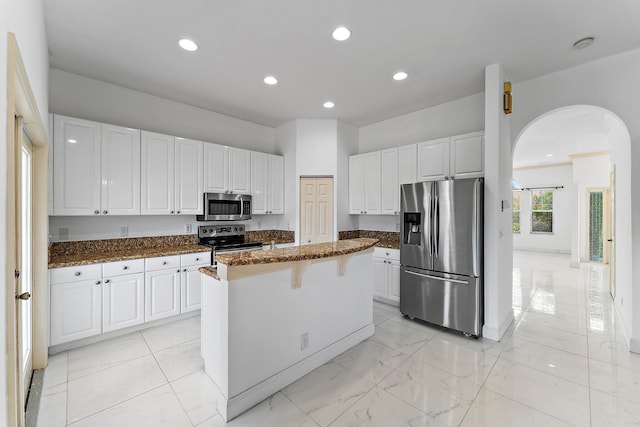 kitchen featuring dark stone counters, a breakfast bar area, a kitchen island, white cabinetry, and appliances with stainless steel finishes