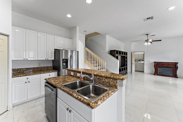 kitchen with appliances with stainless steel finishes, independent washer and dryer, a center island with sink, and white cabinets