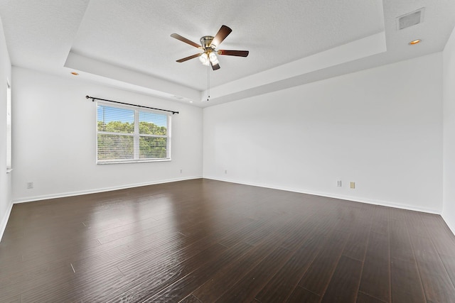 empty room with ceiling fan, a tray ceiling, a textured ceiling, and dark hardwood / wood-style floors