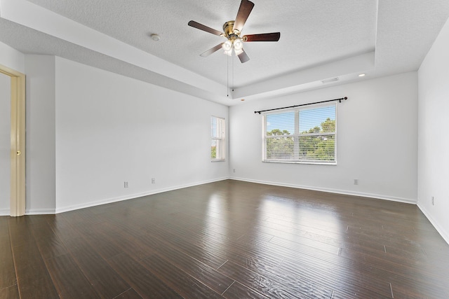 empty room with dark wood-type flooring, ceiling fan, a textured ceiling, and a raised ceiling