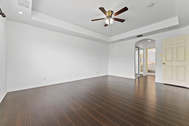 empty room featuring ceiling fan, a tray ceiling, a textured ceiling, and dark hardwood / wood-style floors