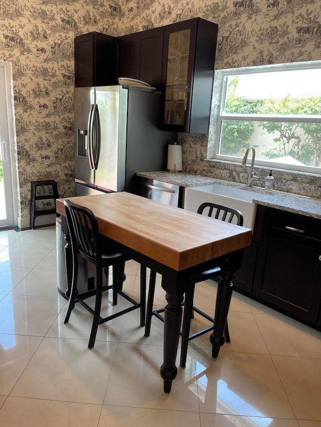 kitchen with dark brown cabinetry, appliances with stainless steel finishes, light stone counters, and light tile patterned flooring