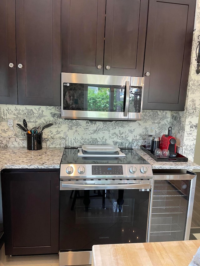 kitchen with appliances with stainless steel finishes, dark brown cabinetry, light stone countertops, beverage cooler, and light hardwood / wood-style flooring