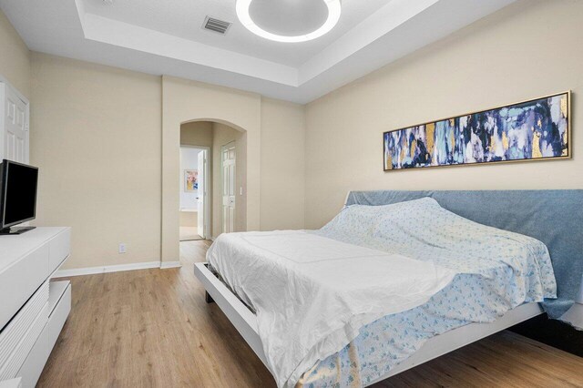 bedroom with light hardwood / wood-style floors and a raised ceiling