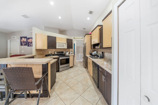 kitchen featuring tasteful backsplash, appliances with stainless steel finishes, a kitchen breakfast bar, lofted ceiling, and tile counters