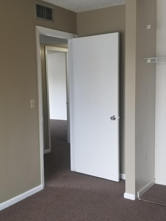 unfurnished bedroom with dark colored carpet, a textured ceiling, and a closet