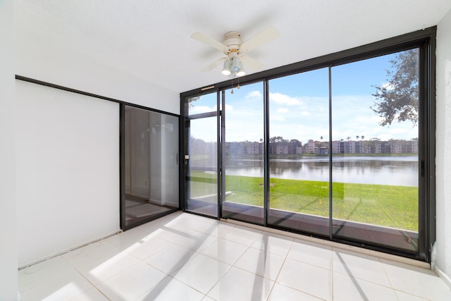 tiled spare room with expansive windows, a water view, and ceiling fan