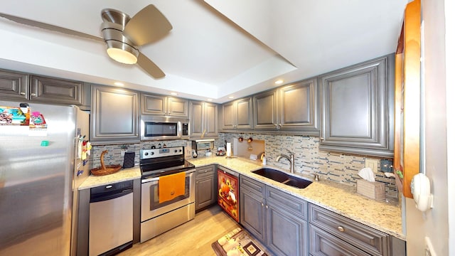 kitchen with sink, light stone countertops, appliances with stainless steel finishes, light hardwood / wood-style floors, and tasteful backsplash