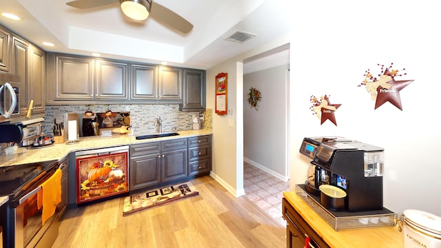 kitchen with light hardwood / wood-style flooring, sink, light stone countertops, a raised ceiling, and tasteful backsplash