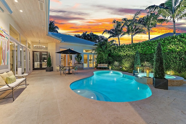 pool at dusk featuring an in ground hot tub, french doors, and a patio area