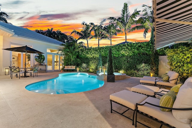 pool at dusk featuring an in ground hot tub and a patio