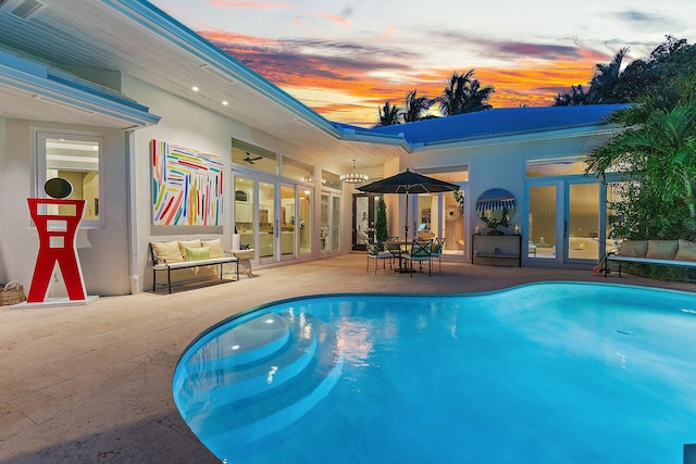 pool at dusk with ceiling fan, a patio area, and french doors