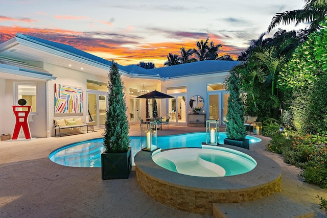 pool at dusk with a patio area and an in ground hot tub