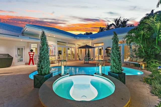 pool at dusk featuring a patio area, an in ground hot tub, and french doors