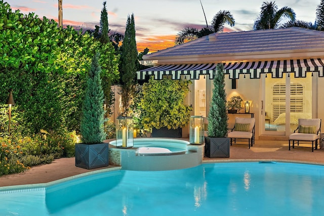 pool at dusk featuring an in ground hot tub and a patio