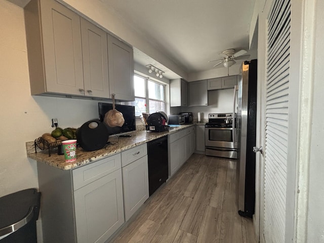 kitchen with light wood-type flooring, ceiling fan, stainless steel appliances, gray cabinets, and light stone counters