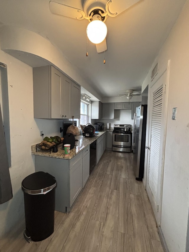 kitchen featuring gray cabinetry, light stone countertops, ceiling fan, stainless steel appliances, and light hardwood / wood-style flooring