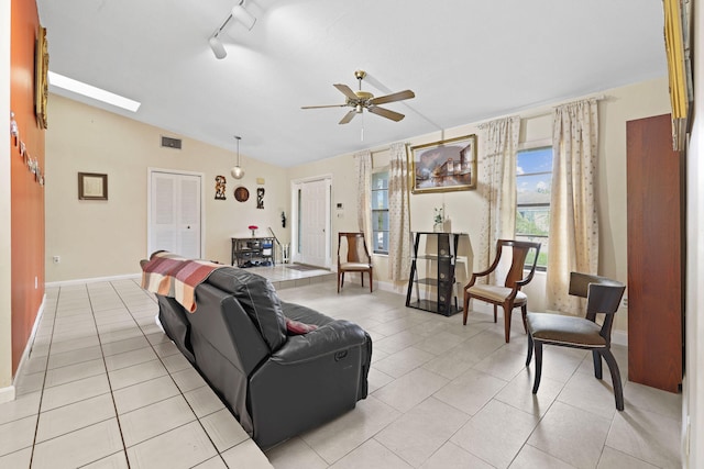 tiled living room with vaulted ceiling with skylight, rail lighting, and ceiling fan