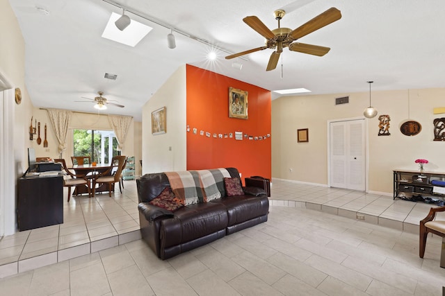 tiled living room featuring vaulted ceiling with skylight, track lighting, and ceiling fan