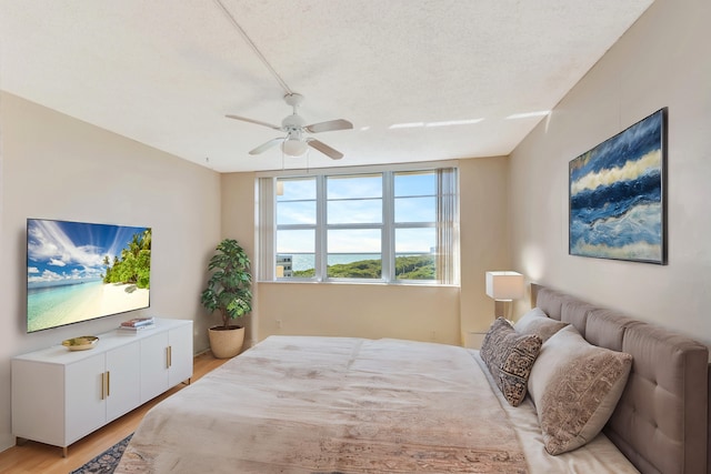 bedroom with ceiling fan, light hardwood / wood-style floors, and a textured ceiling