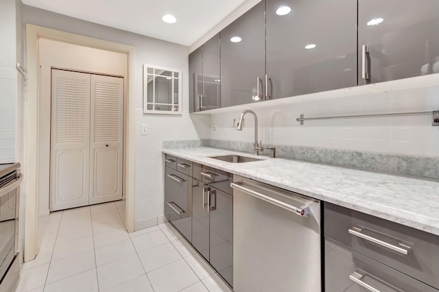 kitchen with sink, stainless steel dishwasher, light stone counters, and gray cabinetry