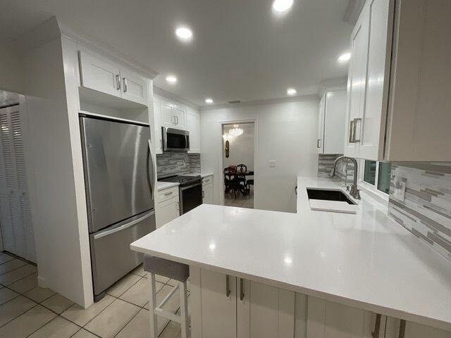 kitchen with white cabinetry, sink, stainless steel appliances, kitchen peninsula, and a breakfast bar